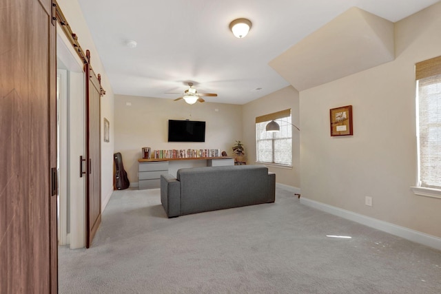 living area featuring light colored carpet, ceiling fan, baseboards, and a barn door