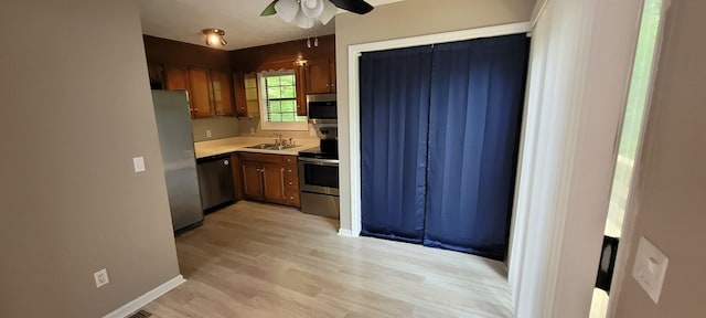 kitchen featuring appliances with stainless steel finishes, light countertops, light wood finished floors, a sink, and a ceiling fan