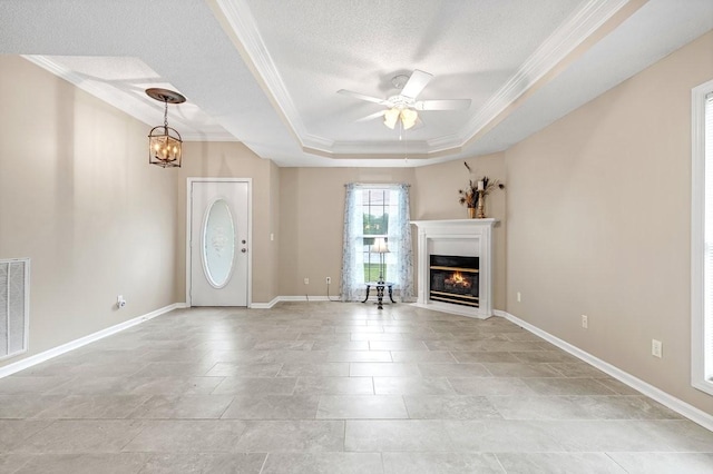 unfurnished living room with a raised ceiling, ceiling fan with notable chandelier, crown molding, and a glass covered fireplace