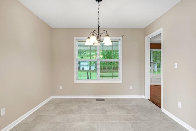 empty room with light tile patterned floors, visible vents, a notable chandelier, and baseboards