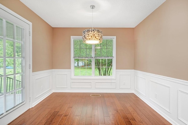 unfurnished dining area featuring visible vents, wainscoting, and wood finished floors
