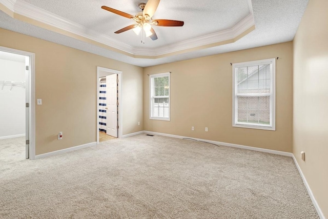 empty room featuring carpet, ceiling fan, a raised ceiling, a textured ceiling, and crown molding