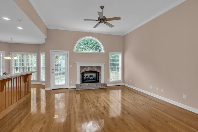 unfurnished living room featuring light wood finished floors, a fireplace, baseboards, ornamental molding, and ceiling fan with notable chandelier