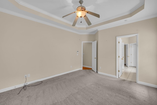 unfurnished bedroom featuring light colored carpet, a tray ceiling, baseboards, ornamental molding, and a ceiling fan