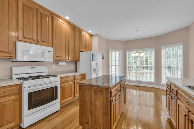 kitchen featuring light wood finished floors, an inviting chandelier, a center island, white appliances, and hanging light fixtures