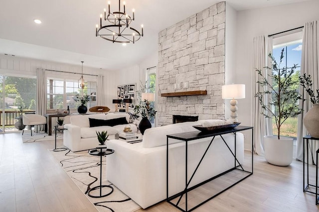 living area with a healthy amount of sunlight, light wood finished floors, a stone fireplace, and a notable chandelier