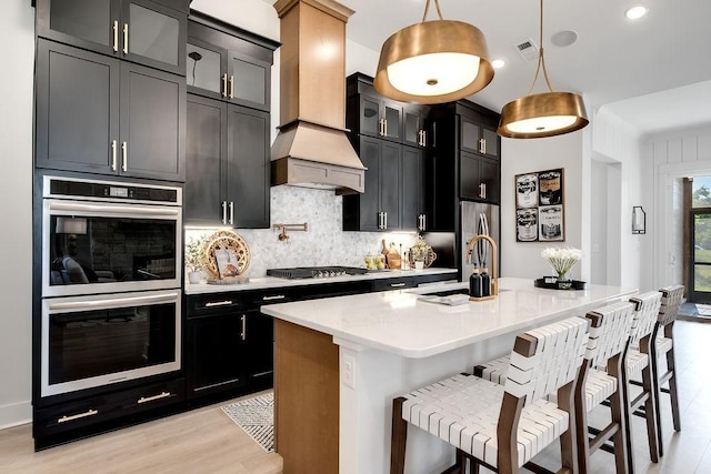 kitchen with decorative backsplash, a center island with sink, dark cabinets, a sink, and appliances with stainless steel finishes
