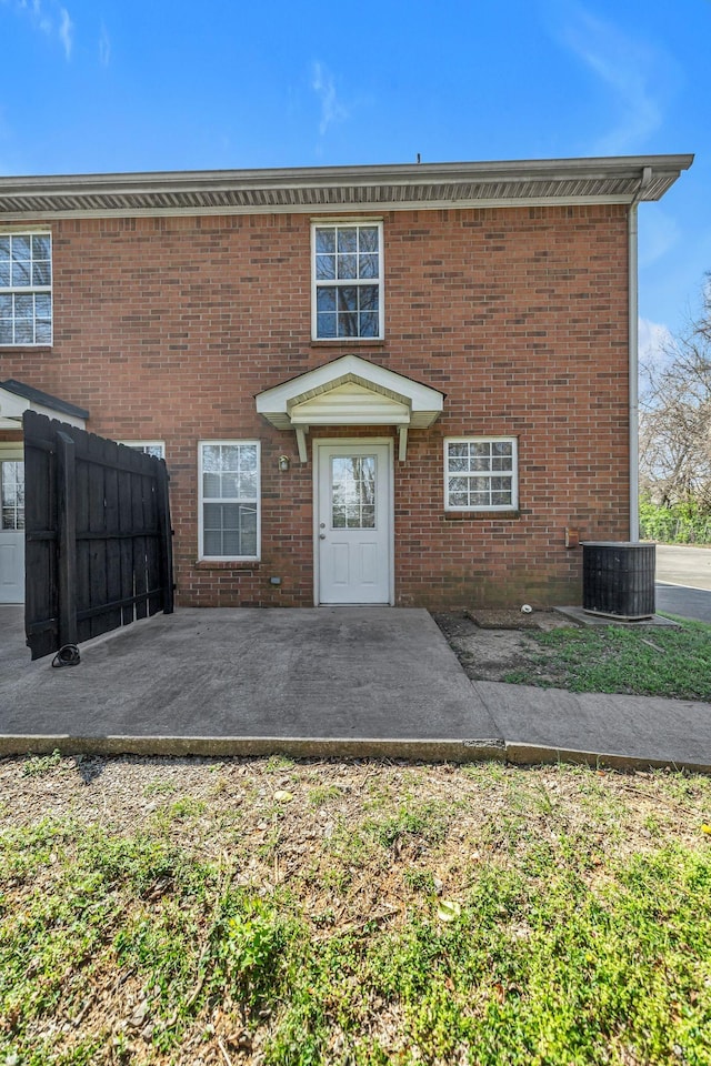 view of front facade featuring fence, central AC unit, brick siding, and a patio