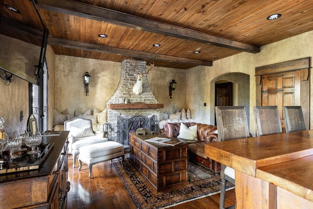 living room featuring recessed lighting, arched walkways, beamed ceiling, a stone fireplace, and wood-type flooring
