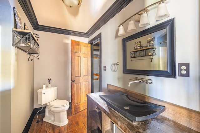 half bathroom featuring wood finished floors, toilet, crown molding, and a sink