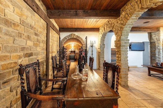 dining space with stone tile floors, arched walkways, beamed ceiling, and wooden ceiling