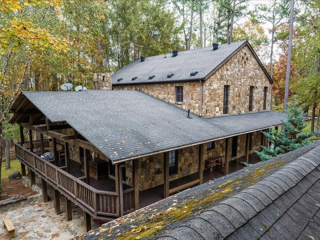 rear view of house featuring roof with shingles and stone siding