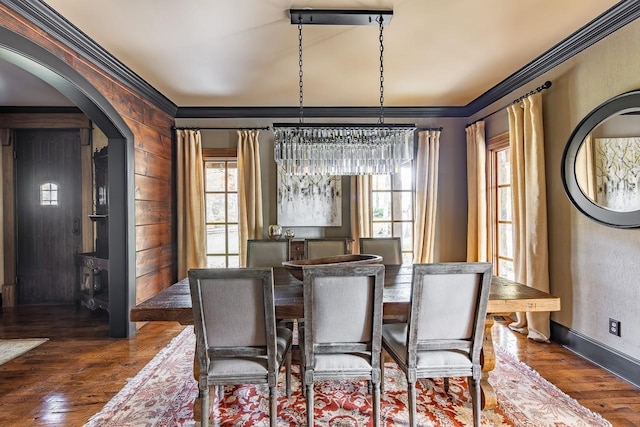 dining space featuring ornamental molding, an inviting chandelier, arched walkways, and dark wood-type flooring
