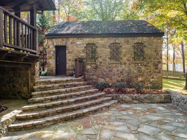 property entrance with a patio, stone siding, and fence