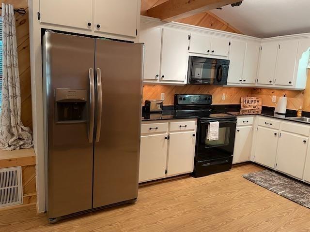 kitchen featuring lofted ceiling, visible vents, dark countertops, black appliances, and light wood finished floors