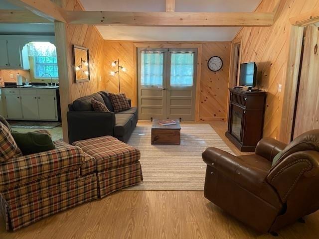 living room featuring beam ceiling, wood walls, light wood-type flooring, and french doors