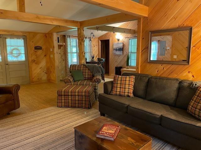 living room with wooden walls, lofted ceiling with beams, and wood finished floors
