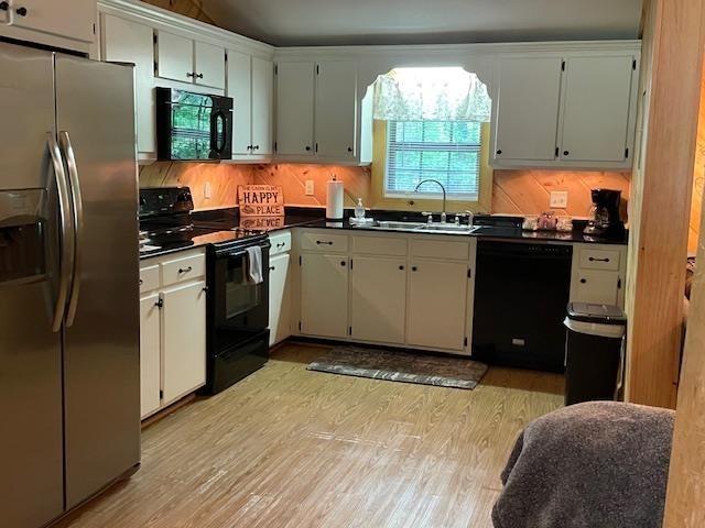 kitchen with black appliances, a sink, dark countertops, and light wood-type flooring