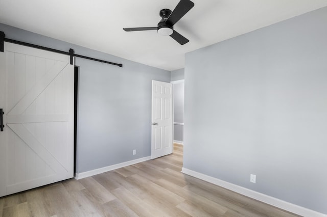 unfurnished bedroom with baseboards, a barn door, wood finished floors, and ceiling fan