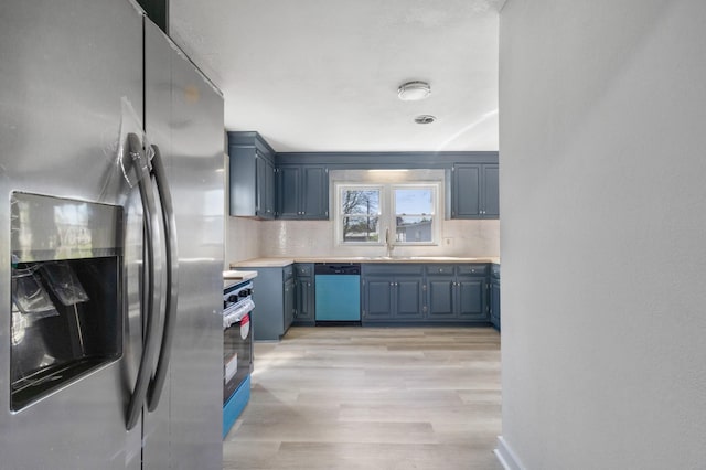 kitchen featuring blue cabinetry, light wood-style flooring, stainless steel appliances, light countertops, and backsplash