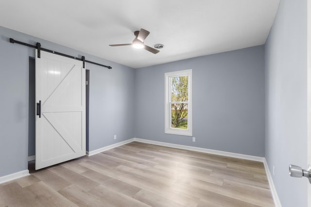 unfurnished bedroom with a barn door, ceiling fan, light wood-style flooring, and baseboards