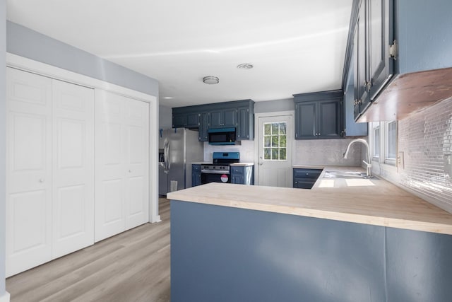 kitchen with light wood-style flooring, a sink, appliances with stainless steel finishes, light countertops, and a peninsula