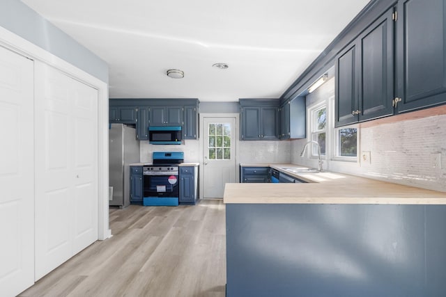 kitchen with a sink, stainless steel appliances, light countertops, light wood-type flooring, and a peninsula
