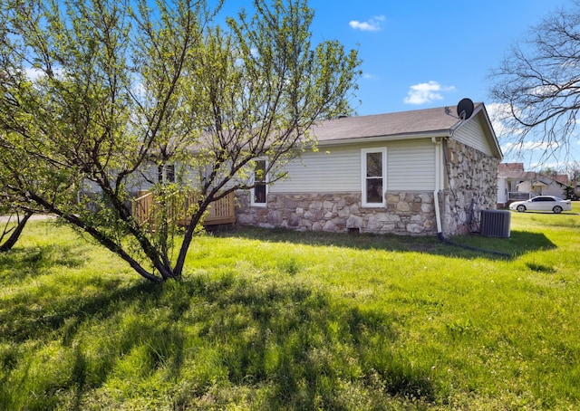 view of side of property featuring central AC unit, a yard, and stone siding