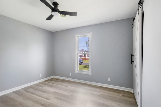 empty room featuring a barn door, ceiling fan, light wood-type flooring, and baseboards