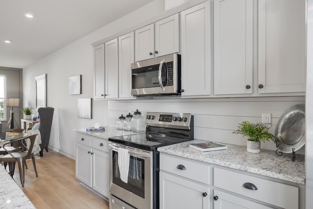 kitchen with recessed lighting, appliances with stainless steel finishes, light wood finished floors, and light stone counters