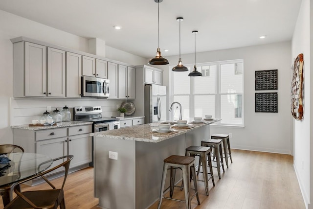 kitchen featuring light stone counters, appliances with stainless steel finishes, a kitchen bar, a kitchen island with sink, and gray cabinets