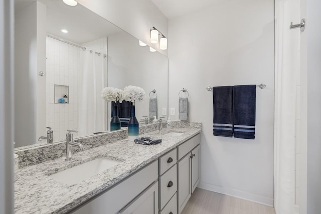 bathroom with a shower with curtain, double vanity, a sink, and baseboards