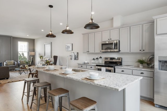 kitchen with a breakfast bar, stainless steel appliances, a sink, light wood-type flooring, and open floor plan
