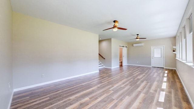 unfurnished living room with stairway, ceiling fan, a barn door, wood finished floors, and a wall mounted air conditioner