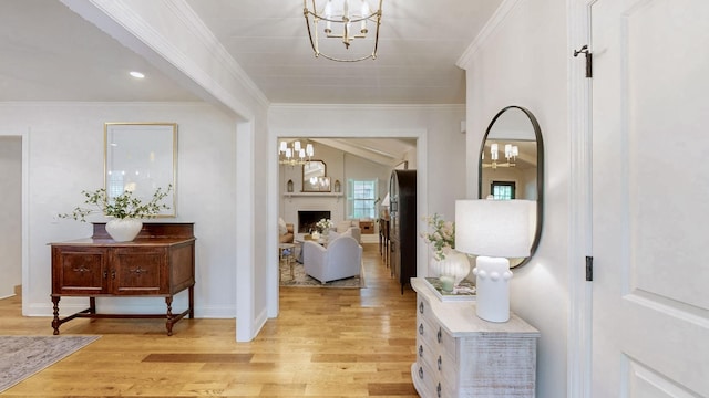 foyer entrance featuring a brick fireplace, a notable chandelier, light wood-type flooring, crown molding, and baseboards