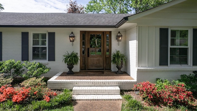 property entrance with board and batten siding, a shingled roof, and brick siding