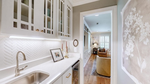 interior space featuring tasteful backsplash, crown molding, light wood-style flooring, a sink, and beverage cooler