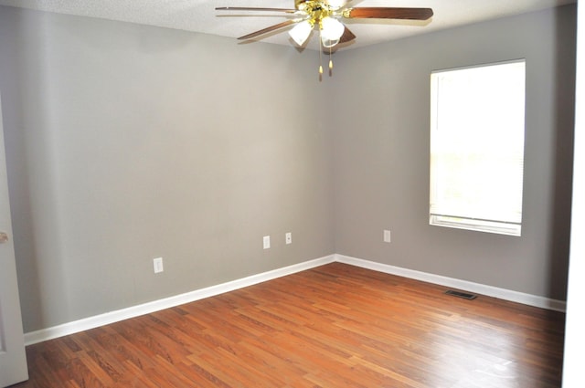 unfurnished room with wood finished floors, visible vents, a ceiling fan, and baseboards