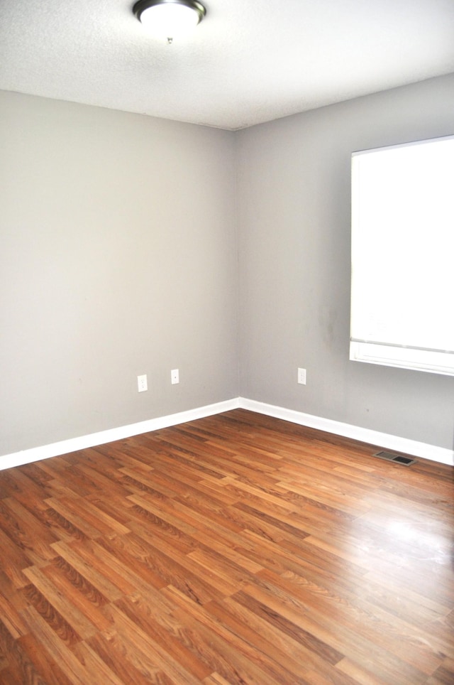 unfurnished room featuring baseboards, visible vents, and wood finished floors