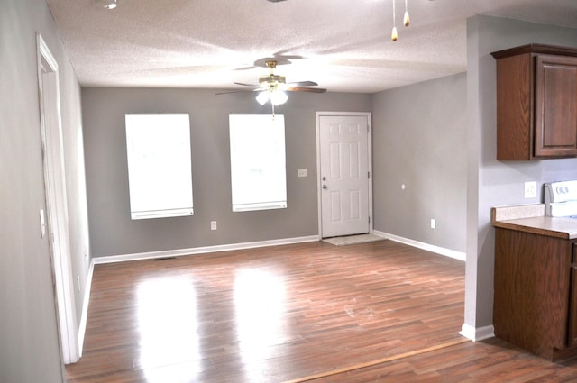 unfurnished living room with wood finished floors, ceiling fan, a textured ceiling, and baseboards
