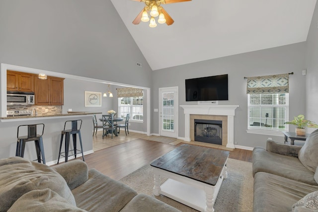 living room with a ceiling fan, visible vents, a fireplace, high vaulted ceiling, and light wood finished floors