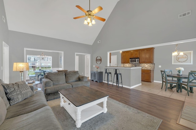 living room with high vaulted ceiling, light wood-style flooring, ceiling fan with notable chandelier, baseboards, and visible vents