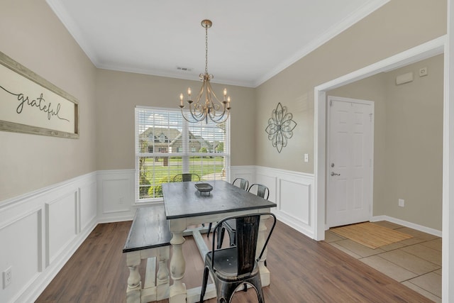 dining room featuring dark wood-style flooring, an inviting chandelier, wainscoting, visible vents, and ornamental molding