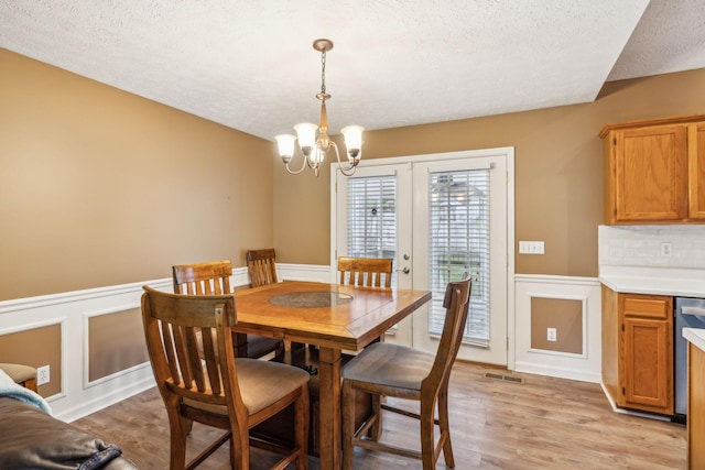 dining space with an inviting chandelier, wainscoting, a textured ceiling, light wood-type flooring, and visible vents