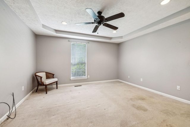 spare room with a raised ceiling, baseboards, a textured ceiling, and light colored carpet