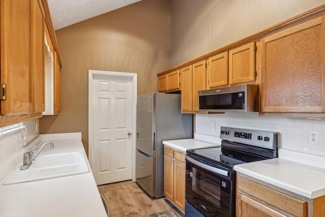 kitchen featuring decorative backsplash, light countertops, a sink, light wood finished floors, and appliances with stainless steel finishes