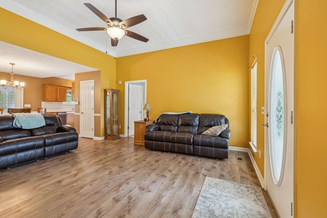 living room with crown molding, light wood-style flooring, ceiling fan with notable chandelier, and baseboards