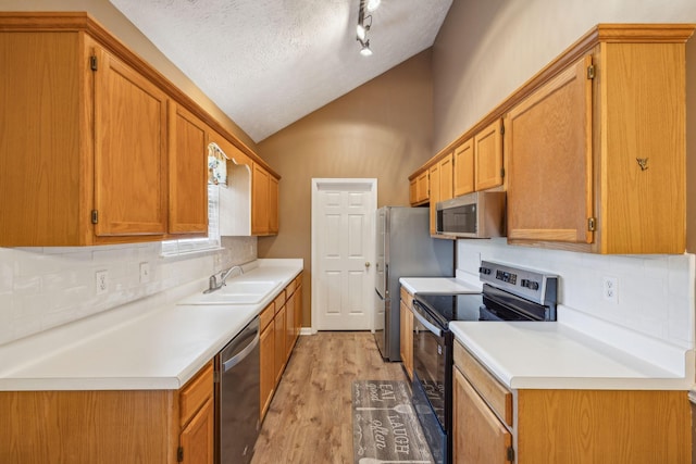 kitchen with decorative backsplash, vaulted ceiling, light wood-type flooring, a sink, and stainless steel appliances