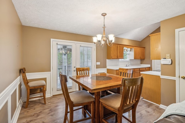 dining room featuring light wood-style floors, a textured ceiling, wainscoting, lofted ceiling, and an inviting chandelier