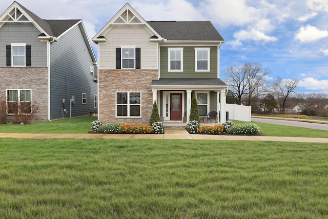 craftsman-style home with a porch, a shingled roof, a front yard, and stone siding